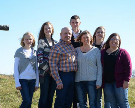 Six people standing together outdoors in a grassy field on a sunny day