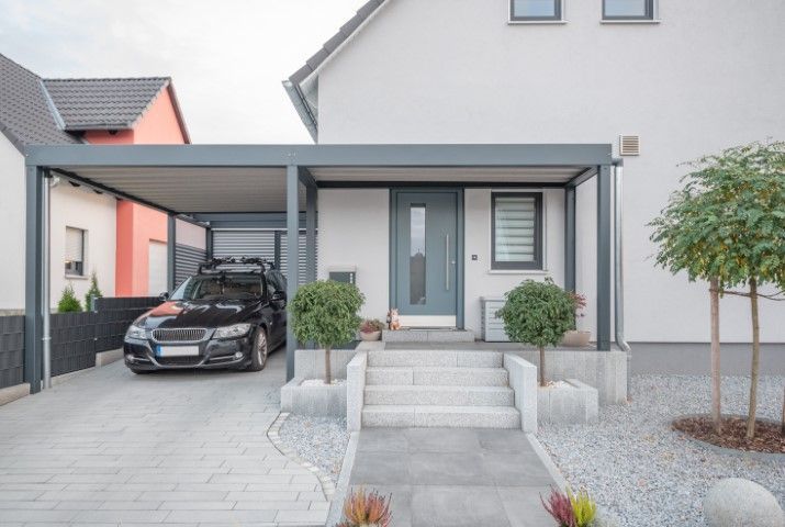 Modern house entrance with carport, black car, gray front door, and landscaped front steps