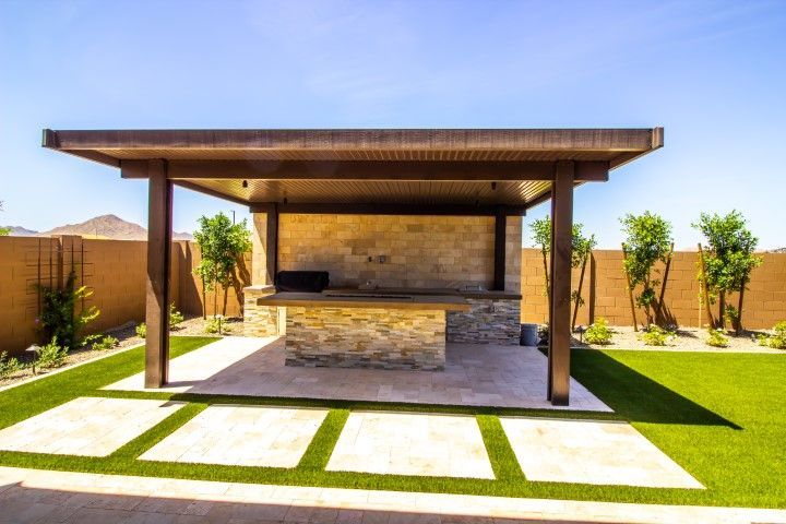 Modern backyard patio with a covered outdoor kitchen, stone counter, and lawn pavers
