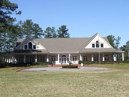 A large white house with a gray roof is surrounded by grass and trees.