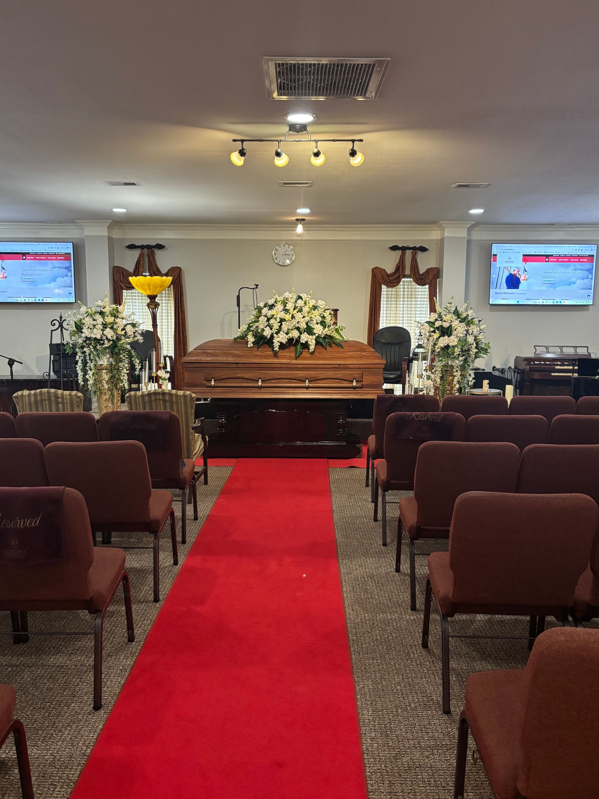 Church funeral service with casket, white flowers, and red aisle between rows of chairs