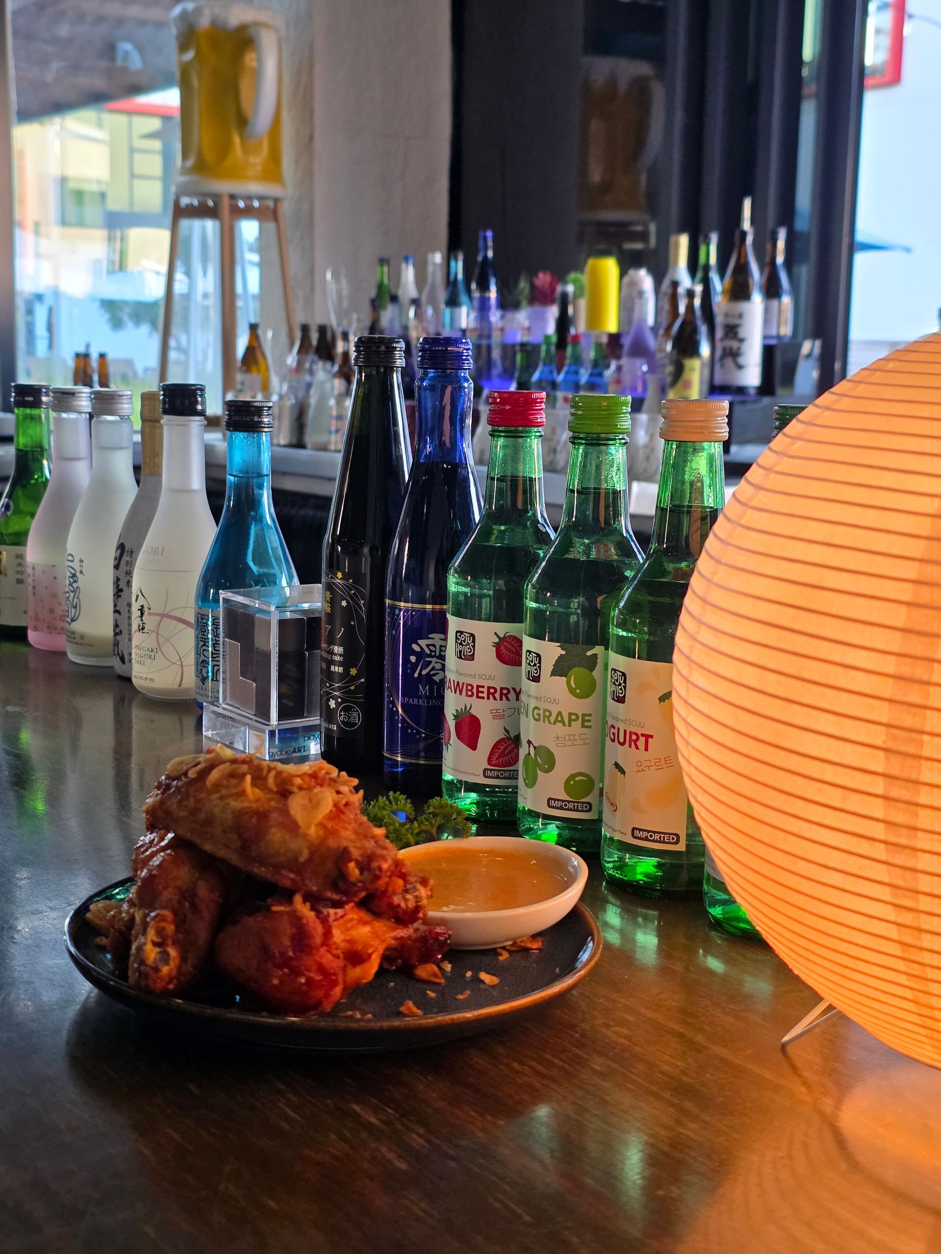 Plates of fried chicken on a bar table with colorful bottled drinks and a glowing lantern nearby