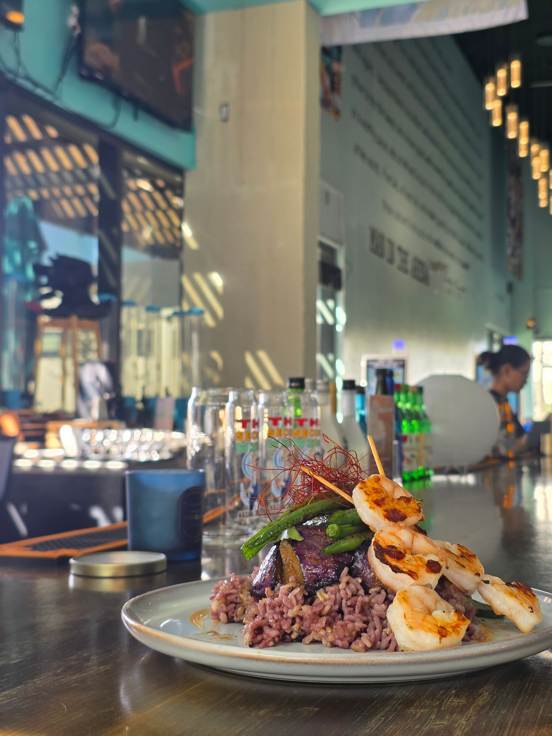 Plate of grilled skewers and rice on a restaurant table with a blurred dining area in the background