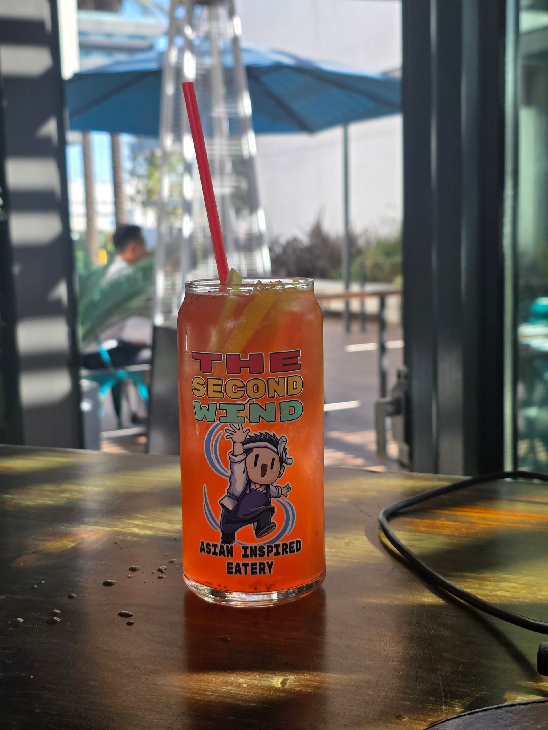 Orange drink cup with a cartoon label and striped straw on an outdoor table by a window
