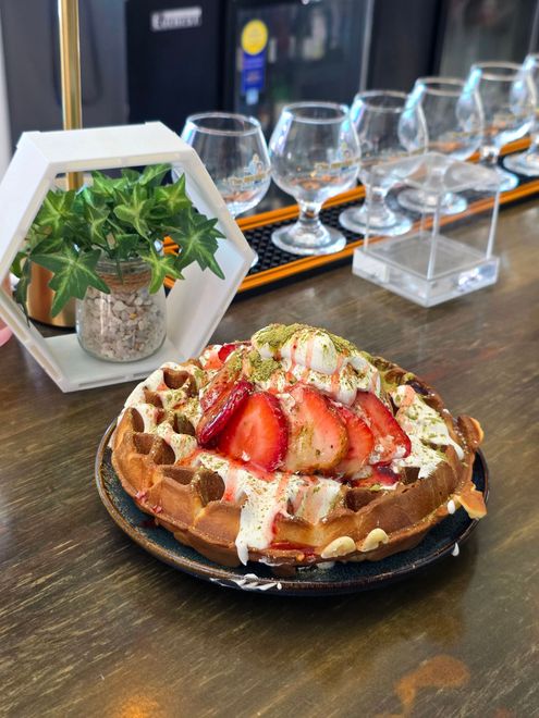 Strawberry waffle topped with cream on a table beside a small plant and wine glasses