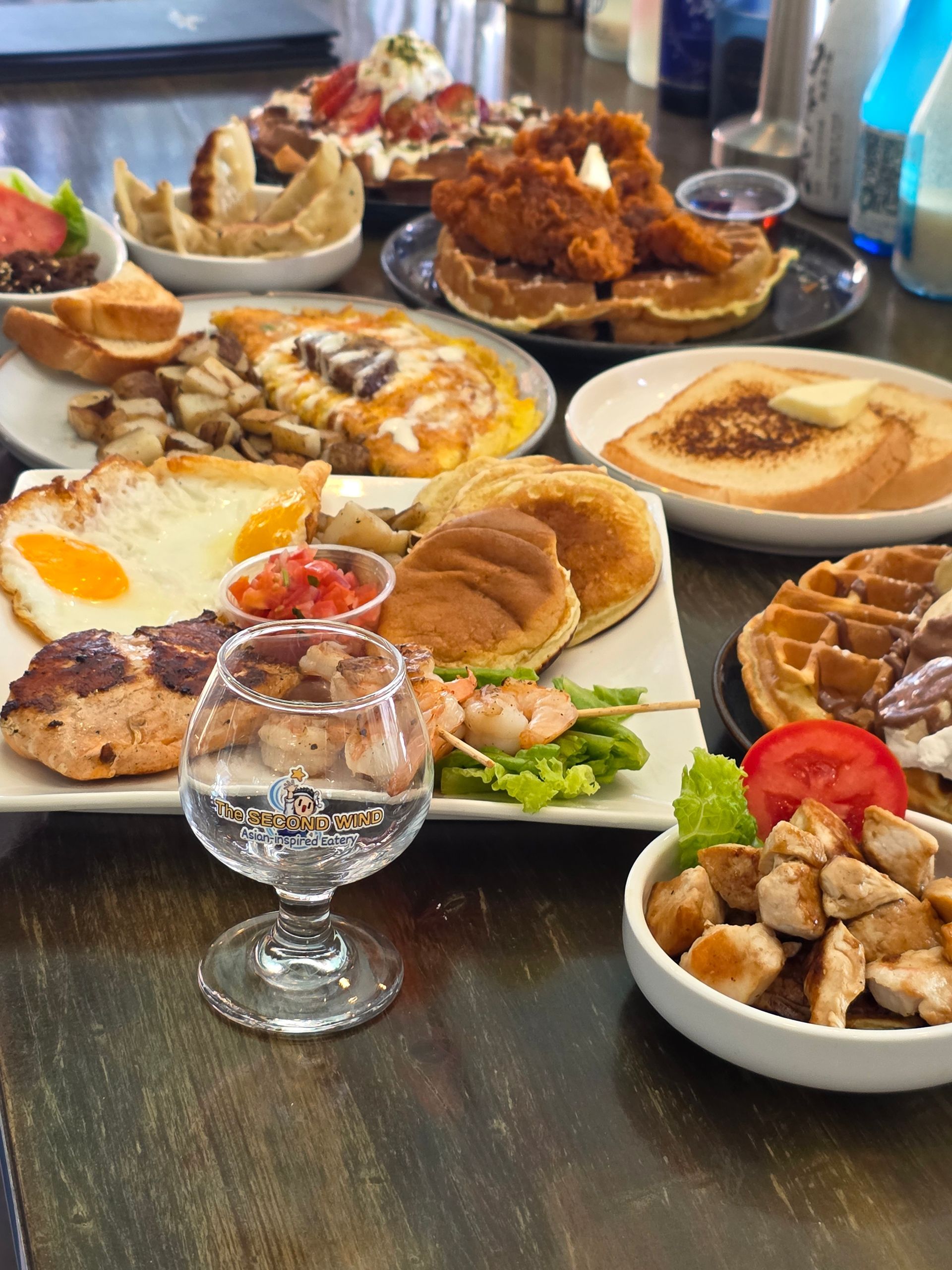 Table full of assorted breakfast dishes, including eggs, waffles, pastries, and coffee cups
