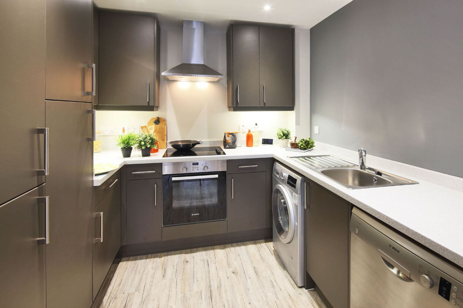 Modern compact kitchen with dark cabinets, white countertops, stainless appliances, and washing machine