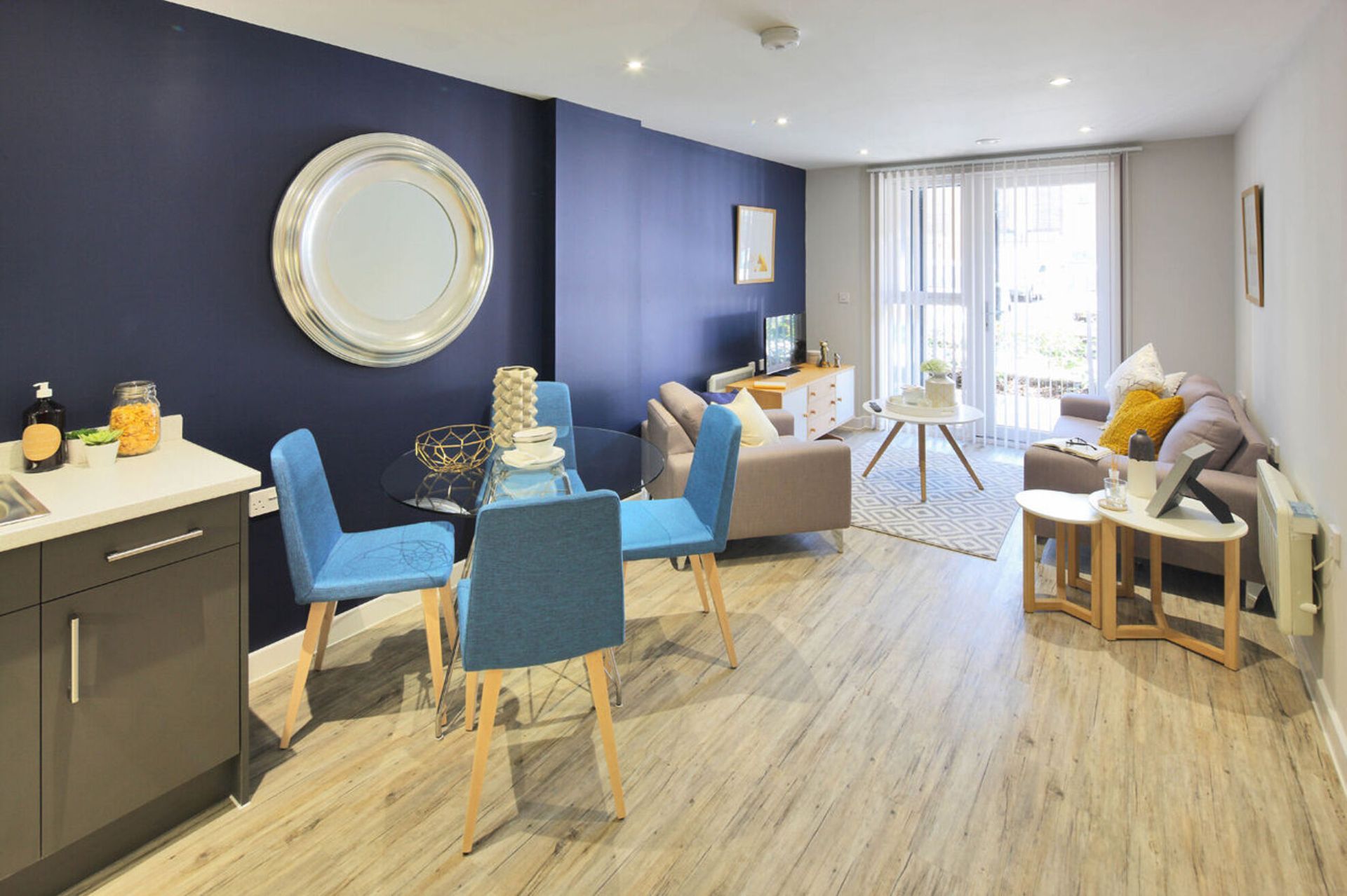 Bright lounge with blue chairs, round table, navy wall, and a sunlit window seating area.