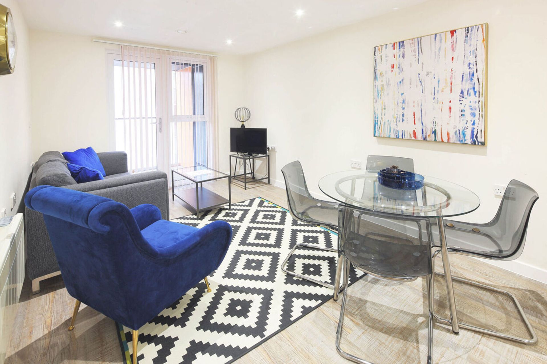 Bright living room with blue sofa, glass dining table, geometric rug, and wall art