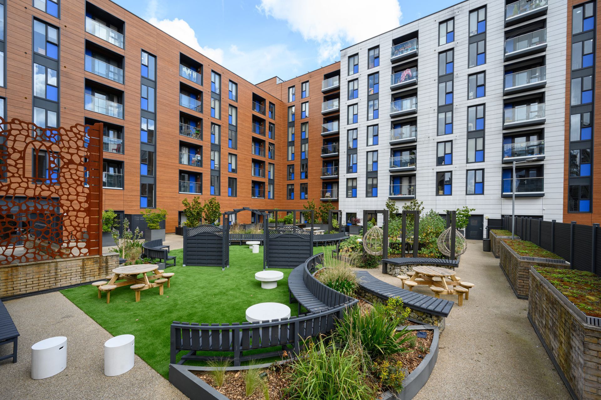 Modern apartment courtyard with green lawn, landscaped paths, and surrounding brick-and-white buildings