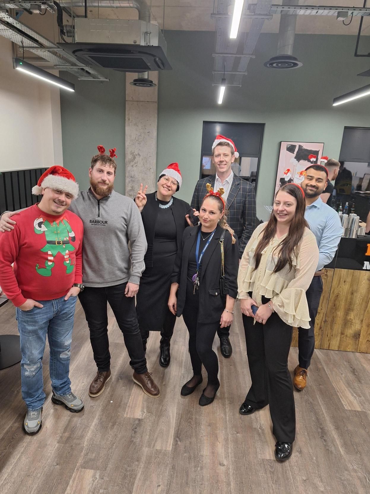 Group of coworkers wearing holiday hats and antlers posing in an office break room