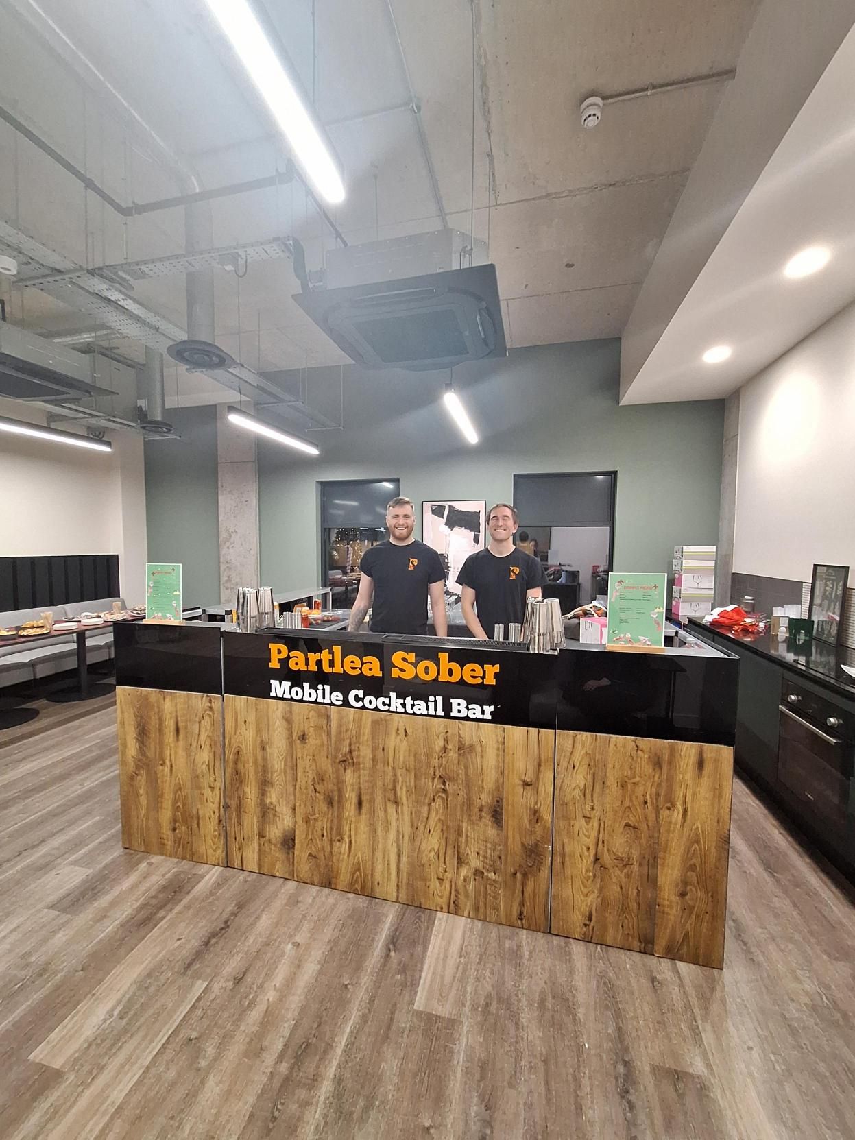 Three people behind a wood-front counter in a modern office lobby with a black sign and wood flooring.