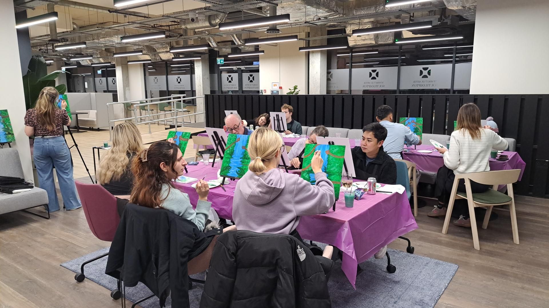 People seated at a purple-covered table in a bright office lounge, chatting and working on green projects.