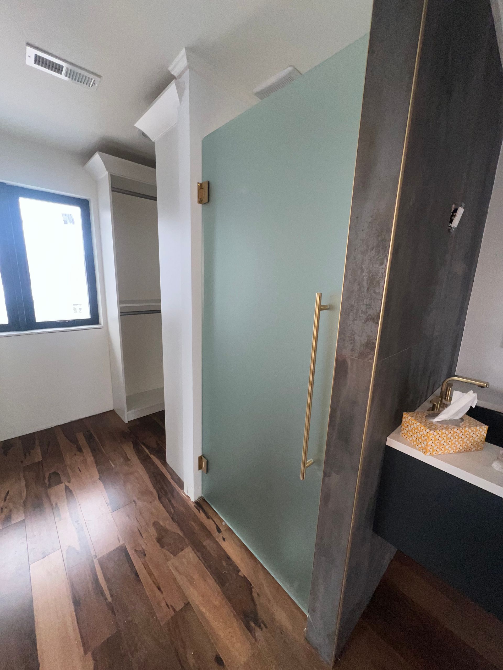 Bathroom with frosted glass shower door, wooden floor, and dark gray vanity. Dearborn Heights