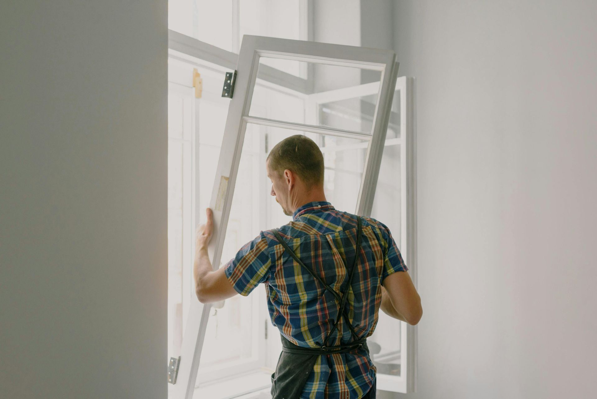 Man holding and installing a window frame in a white-walled room.