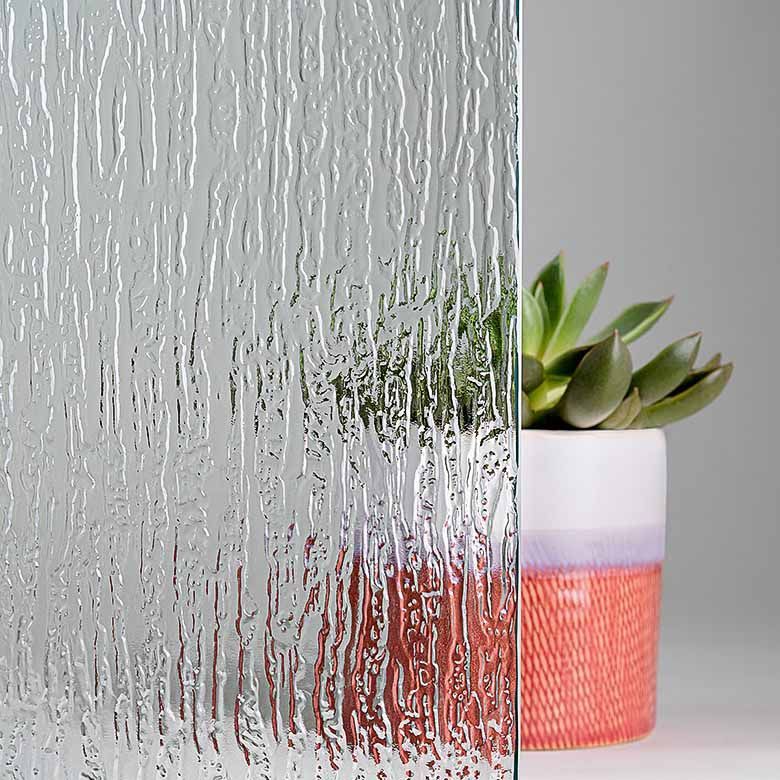 Textured glass panel with vertical grooves, in front of a plant in a coral-colored pot.