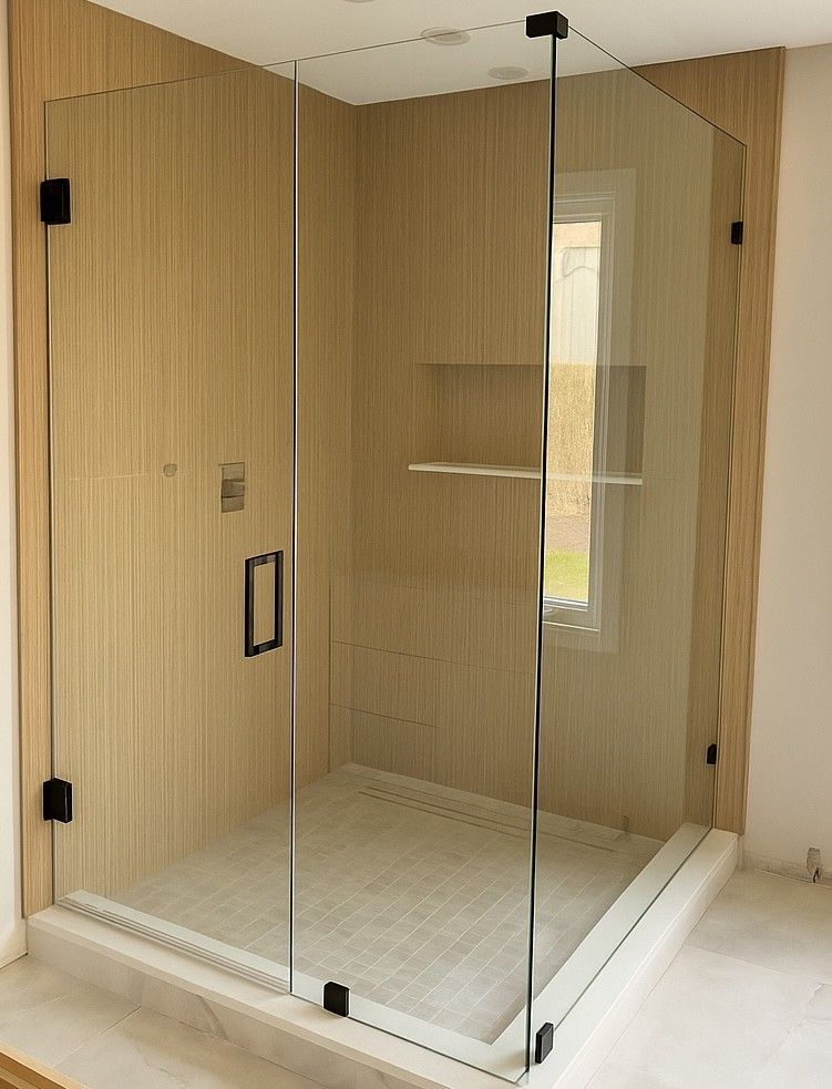 Glass shower enclosure with black hardware, beige tiled walls, and a window. Plymouth