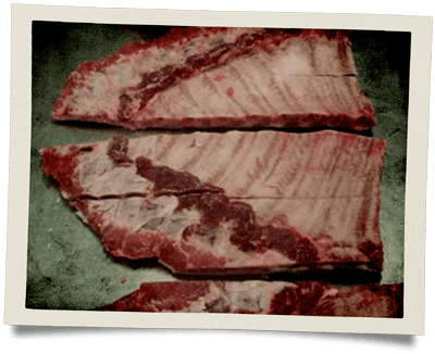 Three strips of raw, bone-in pork spare ribs arranged horizontally on a flat surface.