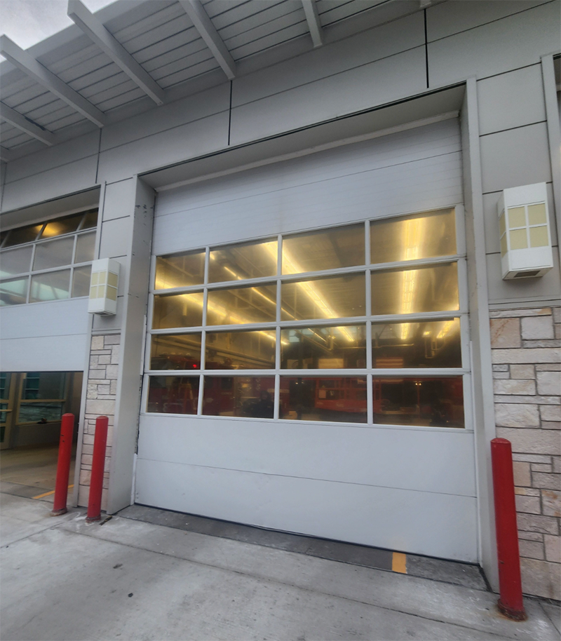 Closed white warehouse garage door with lit interior and red bollards at the entrance