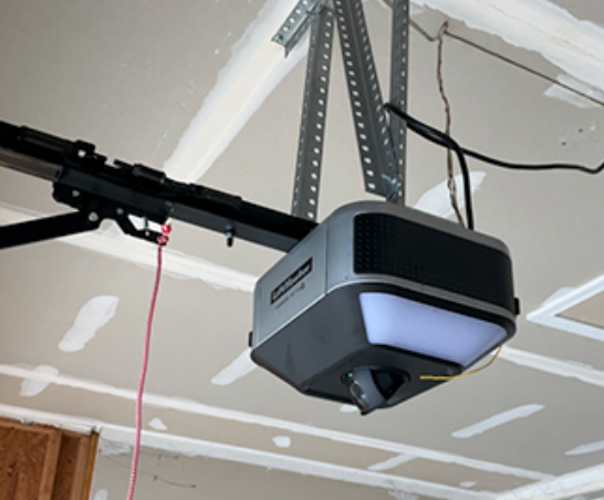 Ceiling-mounted garage door opener with black rail and hanging cables in a garage