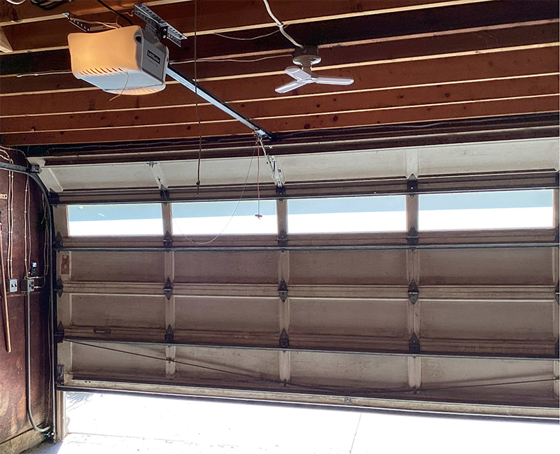 Interior of a garage with a closed brown sectional door and a ceiling-mounted opener above.
