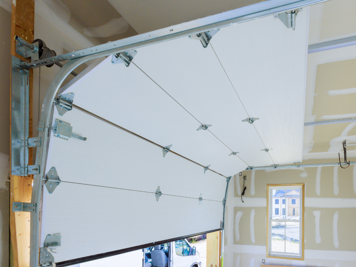 Partially open white sectional garage door inside a new construction garage