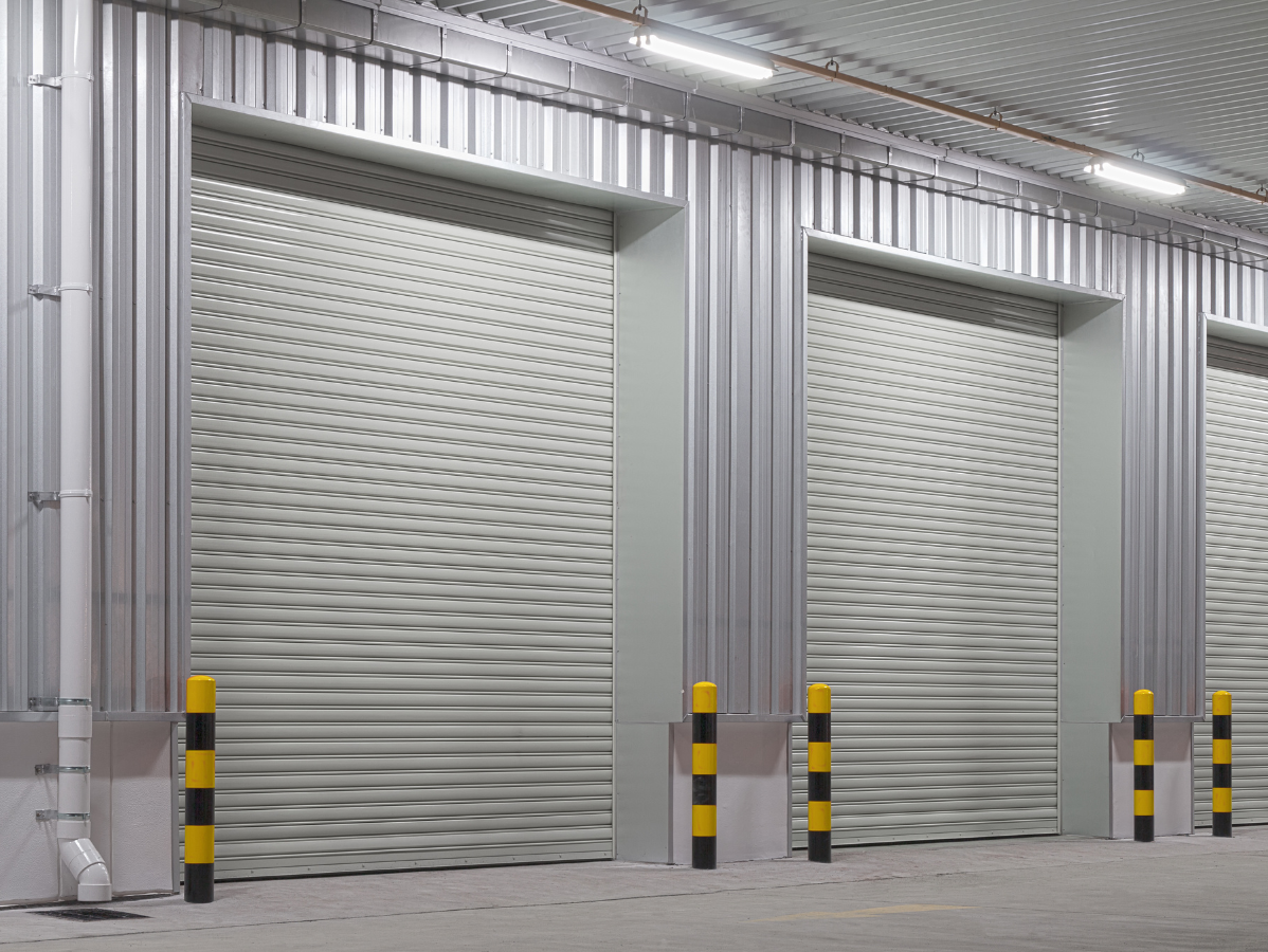 Industrial warehouse with two large metal roll-up doors and yellow-black safety bollards