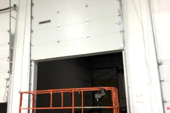 Large white warehouse door partly open with an orange safety barrier in front.