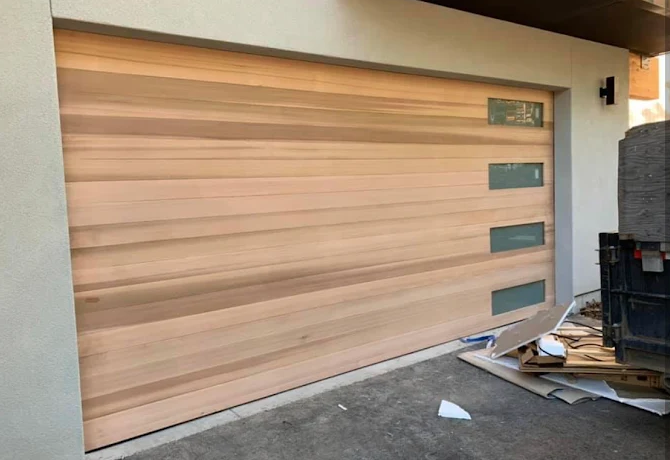 Wooden garage door with narrow windows beside a cluttered driveway and trash bins