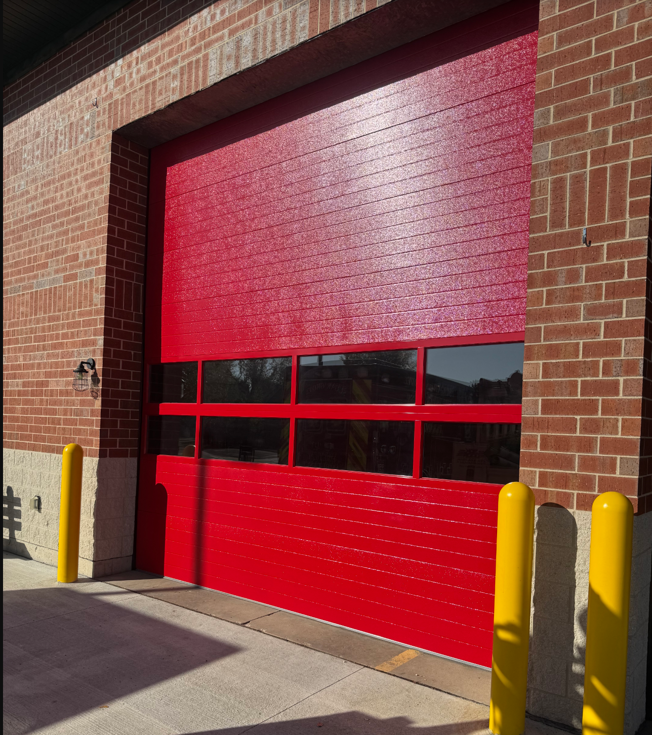 Red roll-up garage door on a brick building with yellow bollards