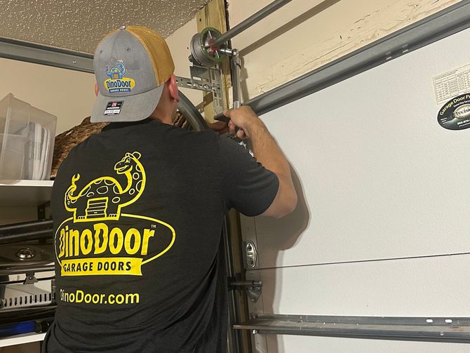 Worker in black SinnoDoor shirt adjusting garage door tracks in a garage.