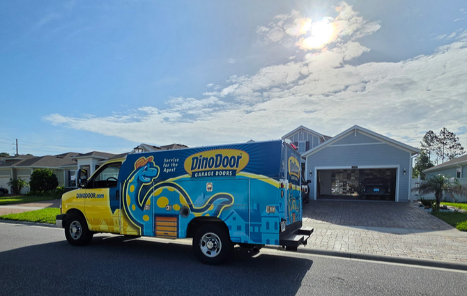 DinoDojo truck parked in a sunny driveway beside a white garage.