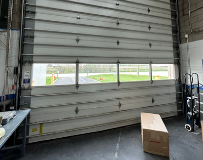 Warehouse loading dock with a partially open roll-up door and a cardboard box on the floor.