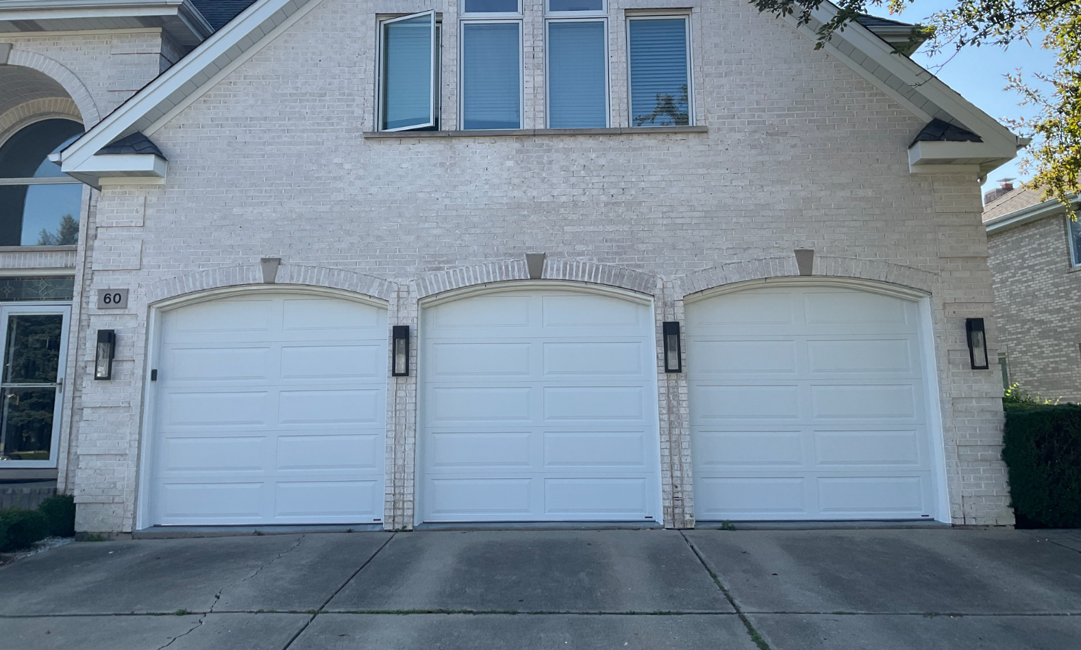 White brick house with three white garage doors and a blue-trimmed upper window.