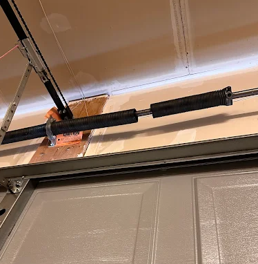 Garage door torsion spring and track hardware mounted above a closed garage door.