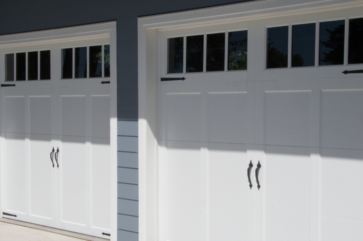 Two white garage doors with small windows on a house exterior