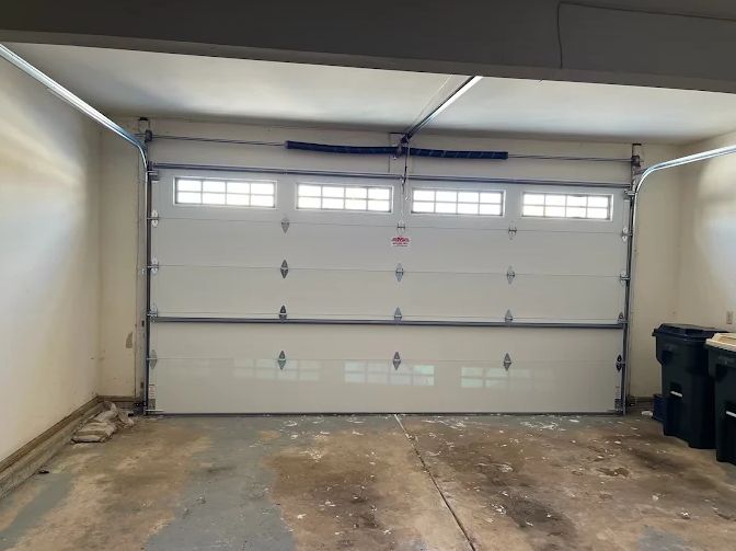 Empty two-car garage with a white door, concrete floor, and trash bins on the right.