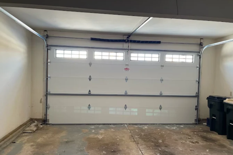 Empty residential garage with a closed white door and two trash bins on the right.