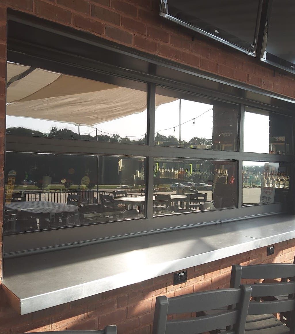 Outdoor bar with large windows, reflecting outdoor tables and awning. Stainless steel bar top.