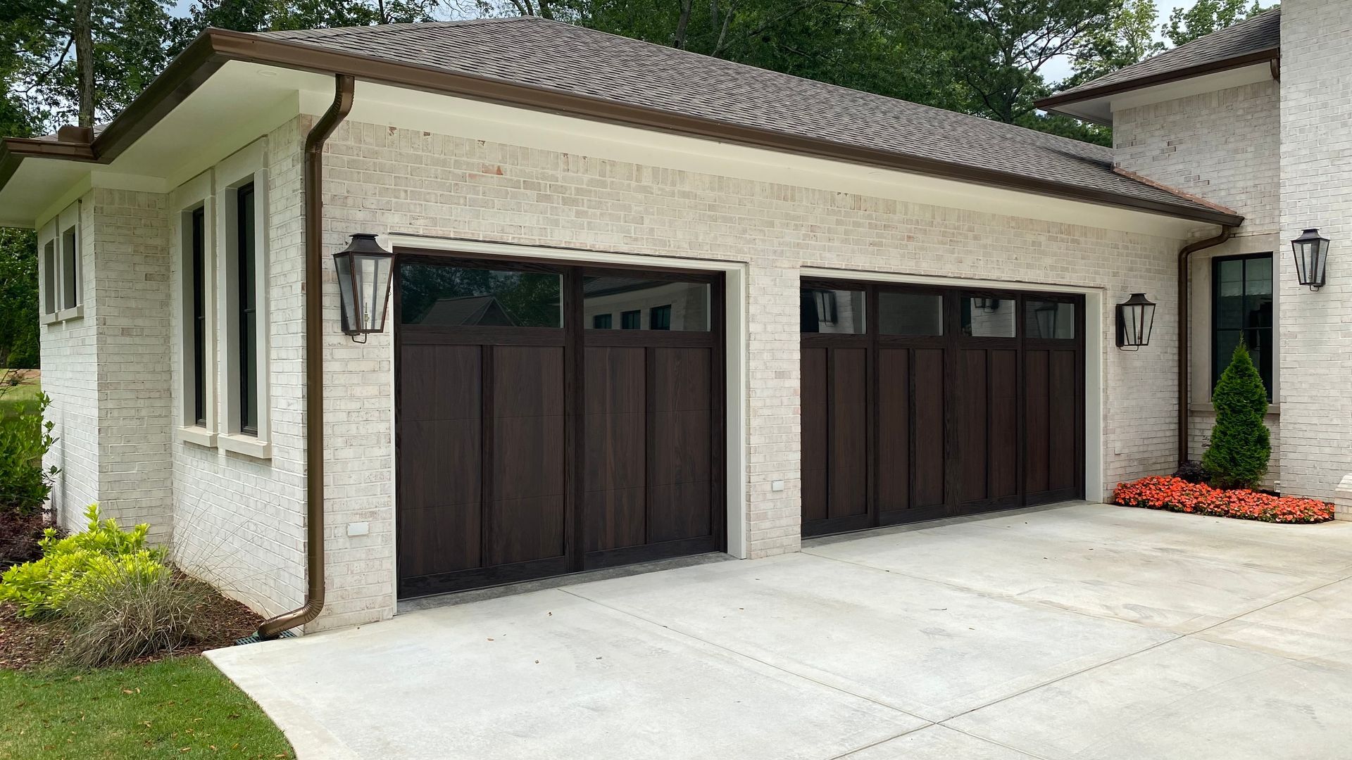Garage with two dark brown doors, light stucco walls, and brown gutters.