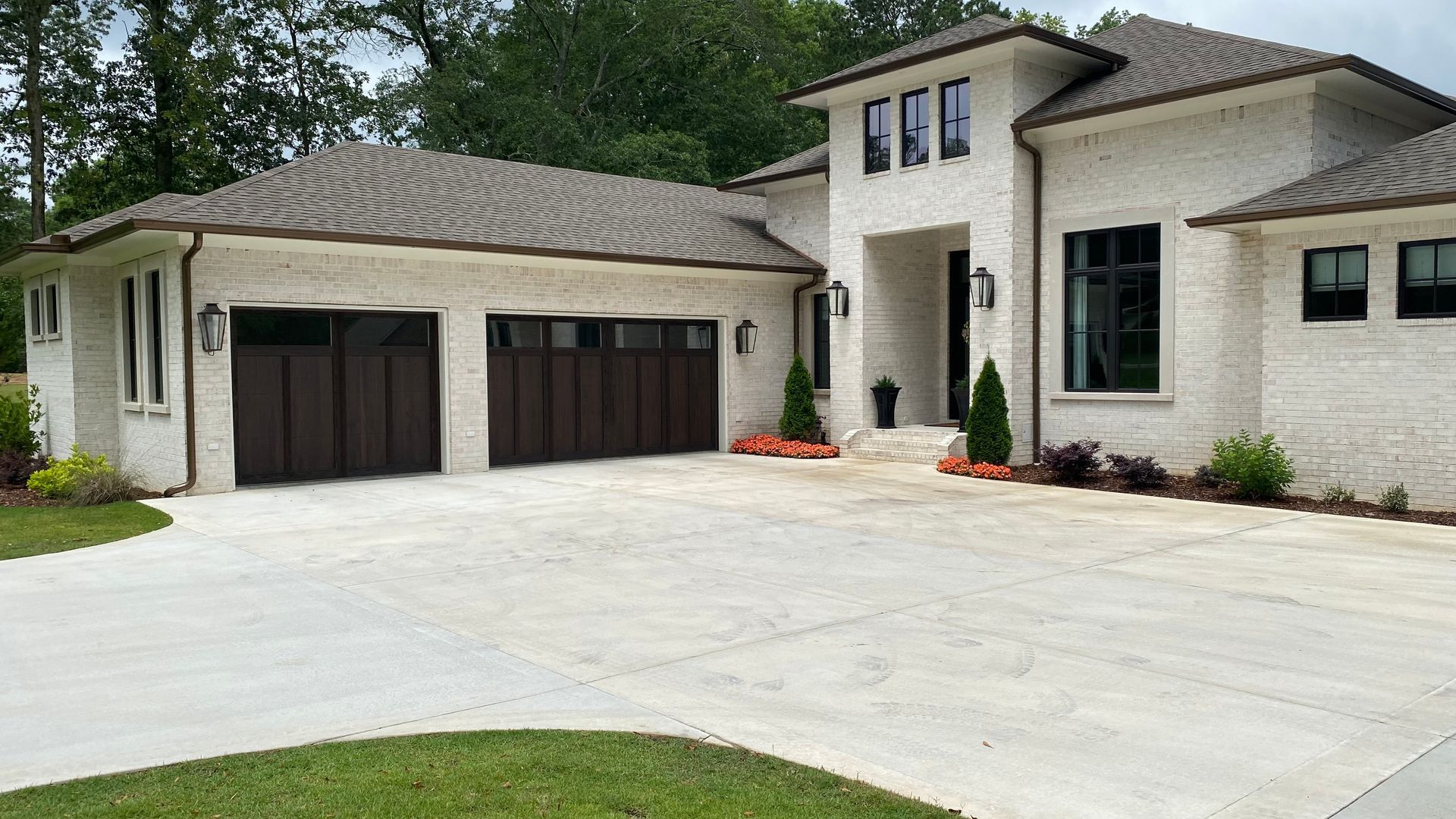 White stucco house with brown garage doors and roof, concrete driveway.