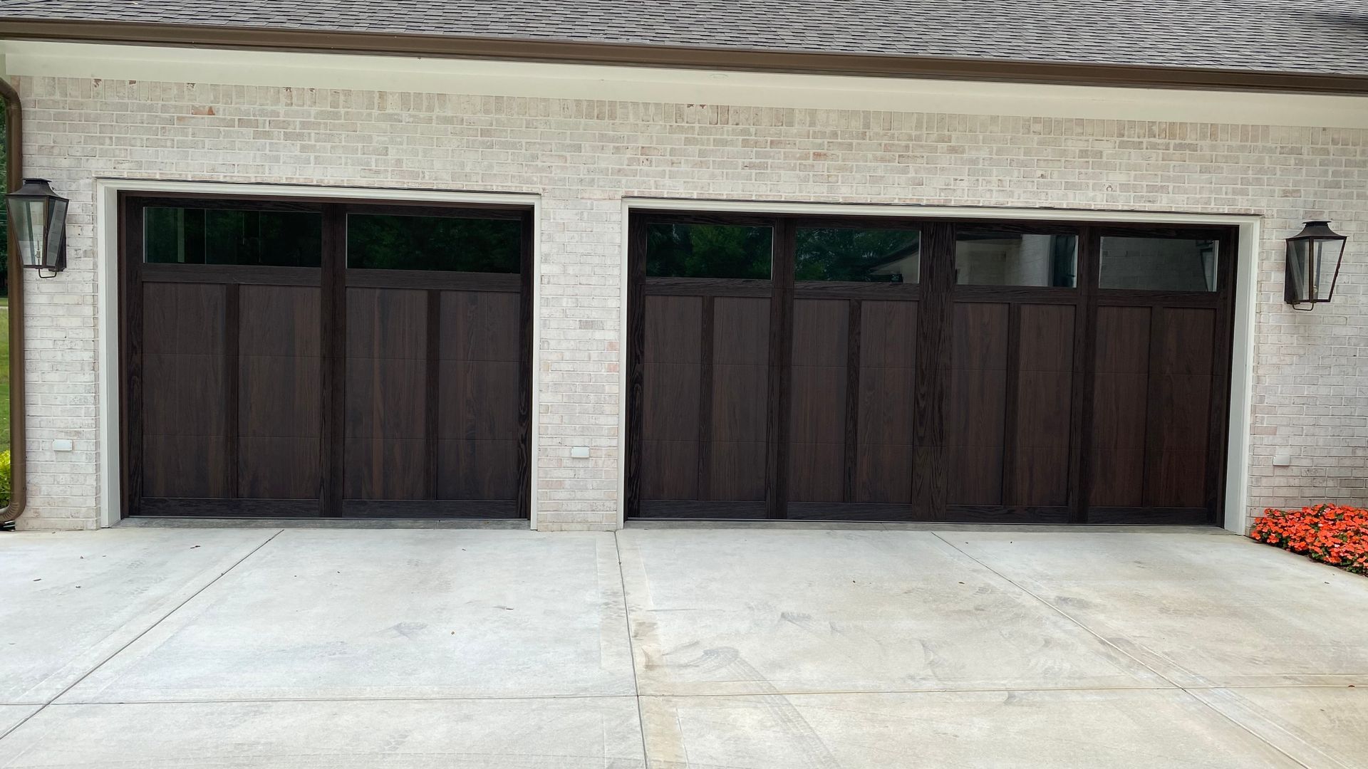 Two dark brown garage doors with glass panels in a brick building.