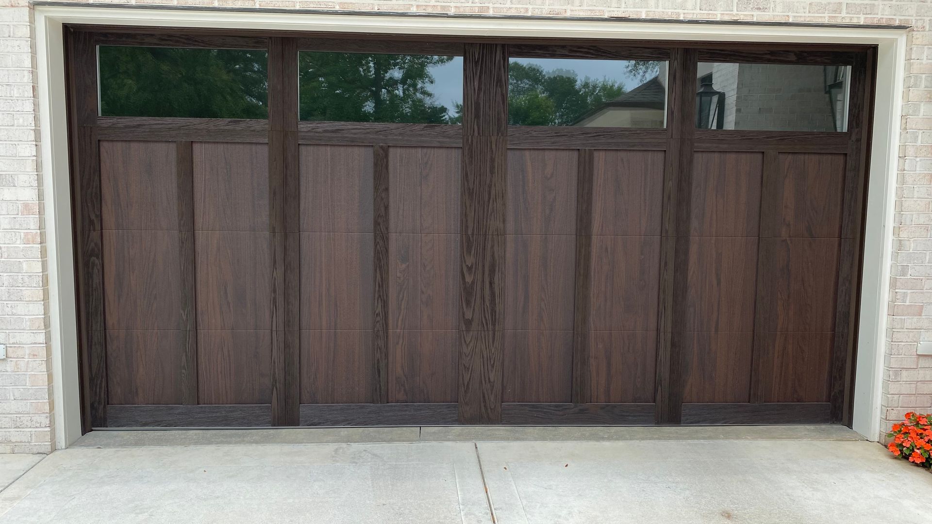 Brown wooden garage door with windows, set in a brick frame on a concrete driveway.