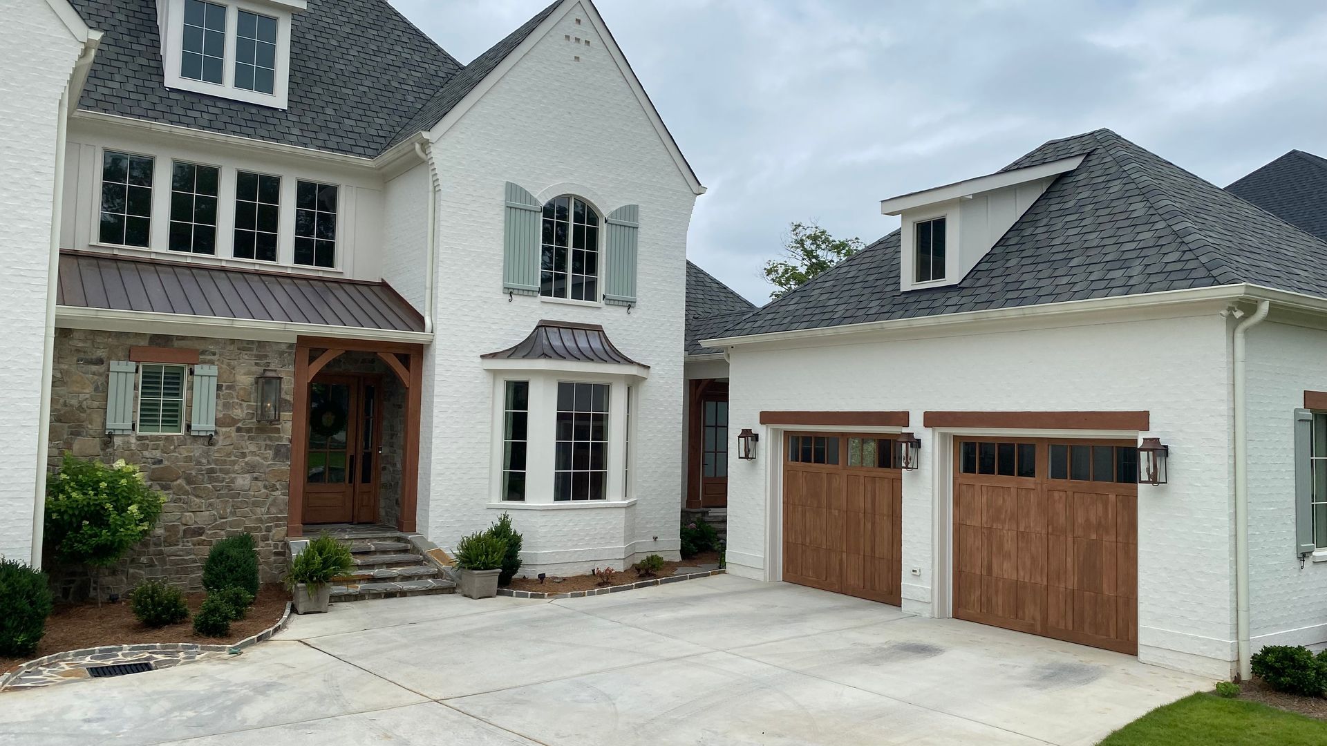 White brick house with dark gray roof and brown garage doors. Driveway in front.