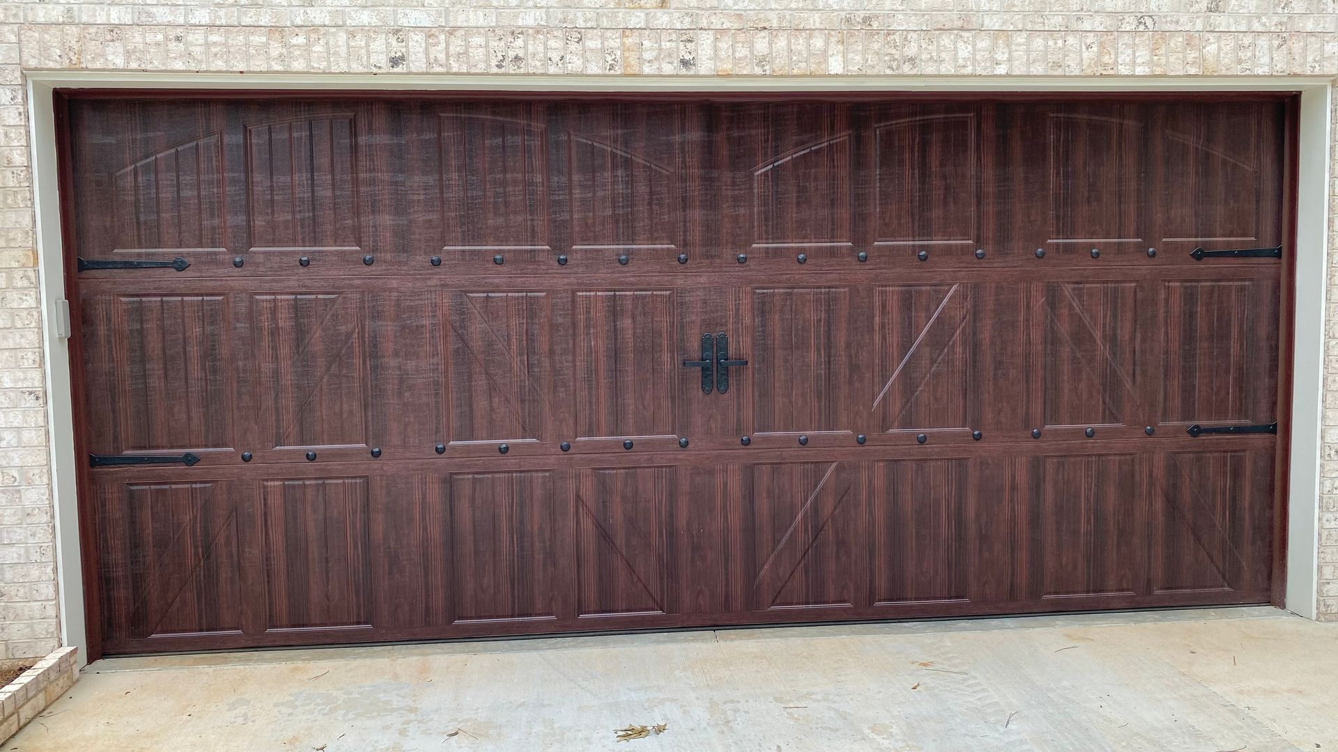 Brown garage door with decorative hardware against a white brick building.