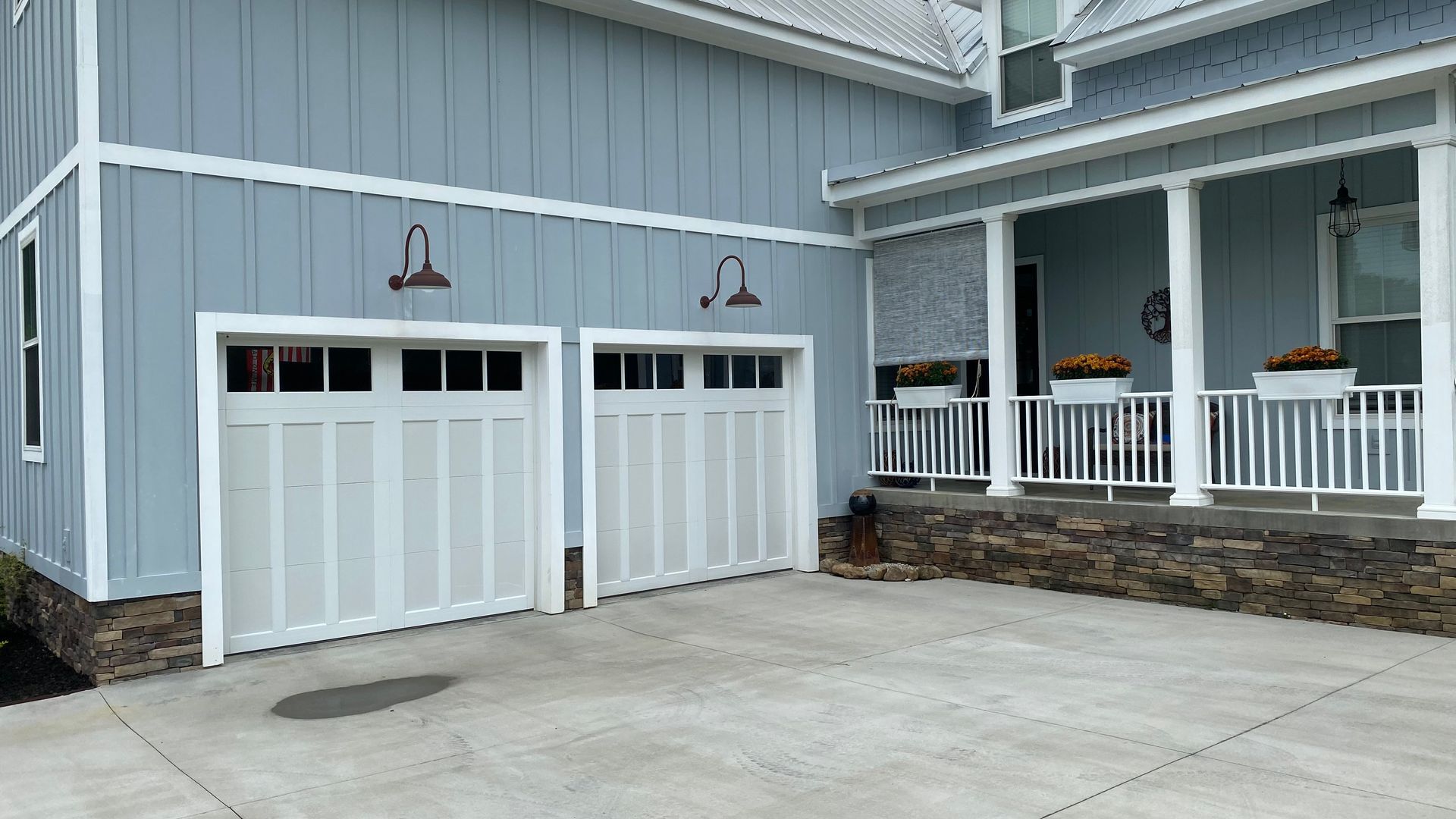 Blue house with white garage doors and a porch, set on a concrete driveway.