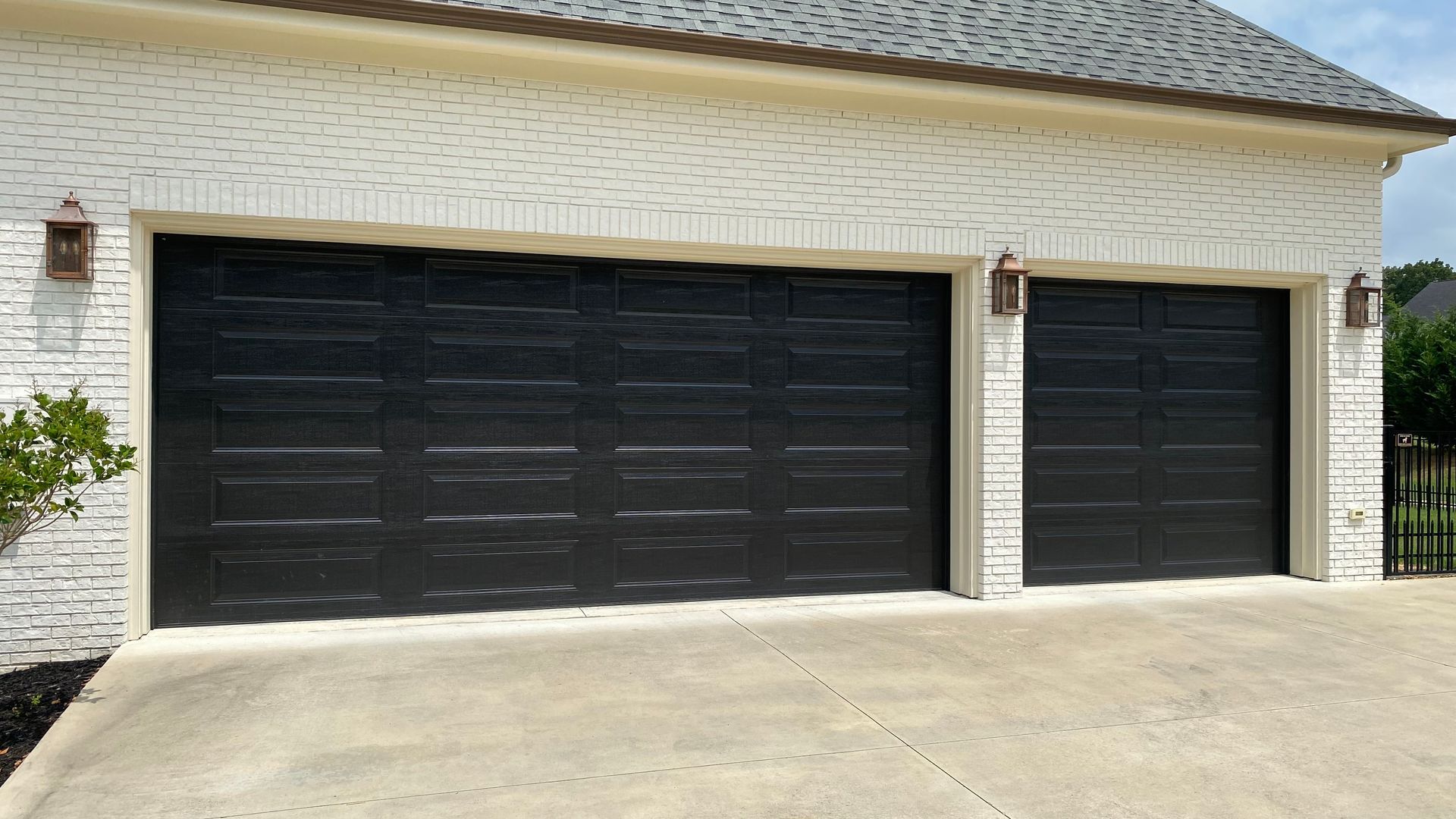 Two black garage doors on a house with white brick exterior and concrete driveway.