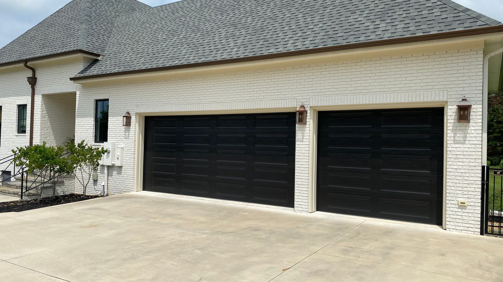 Two-car garage with black doors, white brick exterior, and gray shingle roof.