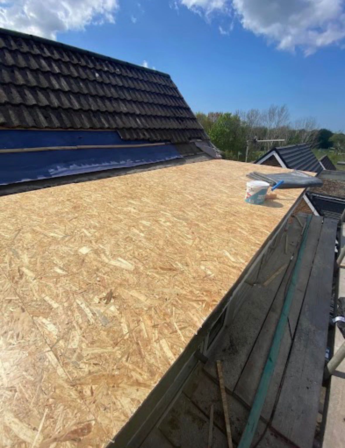 A high-angle view looking down at a newly tiled reddish-brown roof with a chimney, next to a scaffolded section.