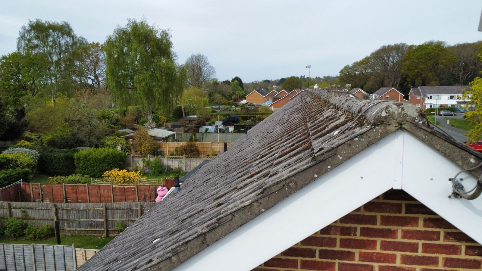 Residential rooftops and trees in a suburban neighborhood, with a brick gable roof in the foreground.